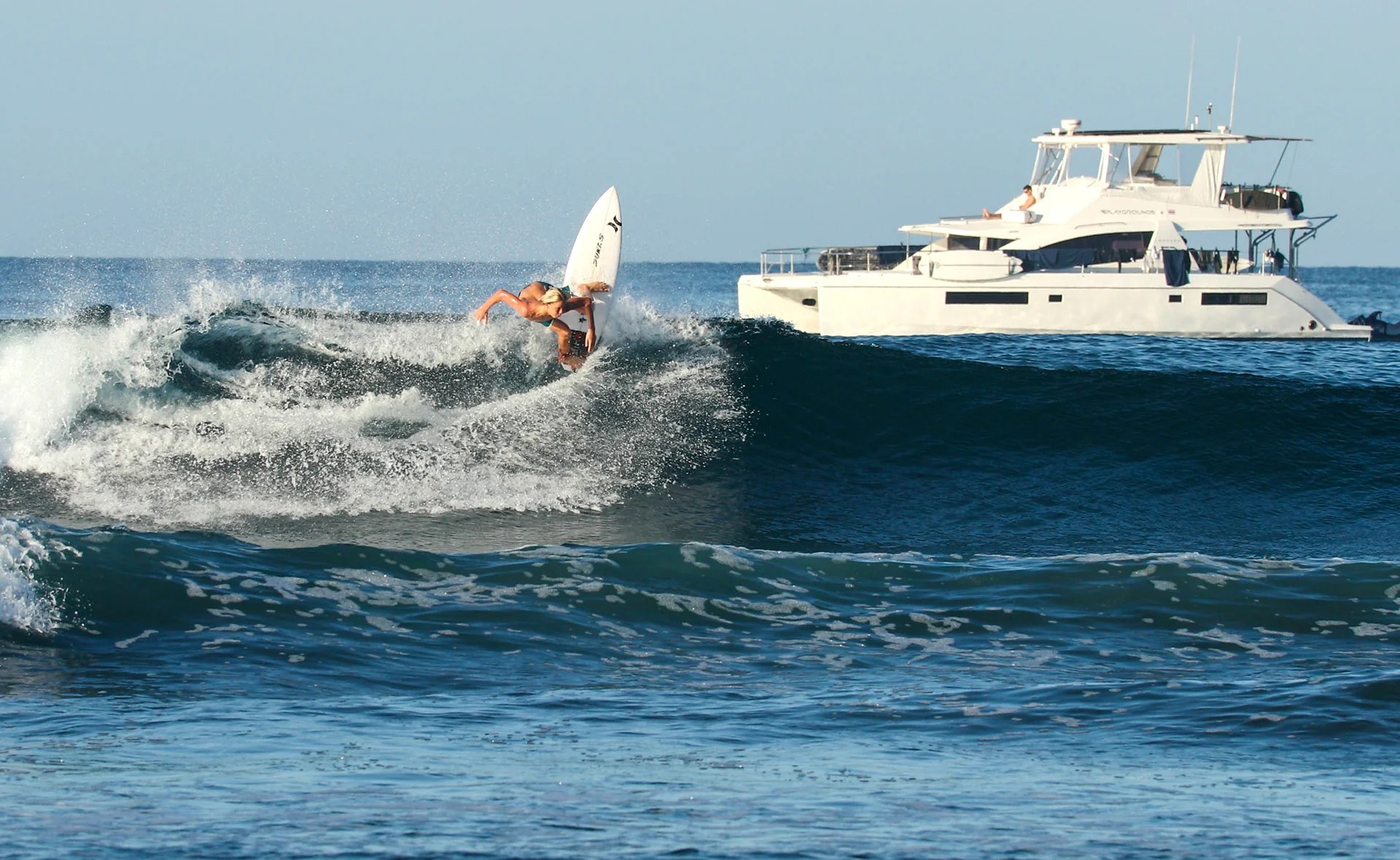 Surfer riding a wave beside the Playgrounds catamaran off Tamarindo, Costa Rica